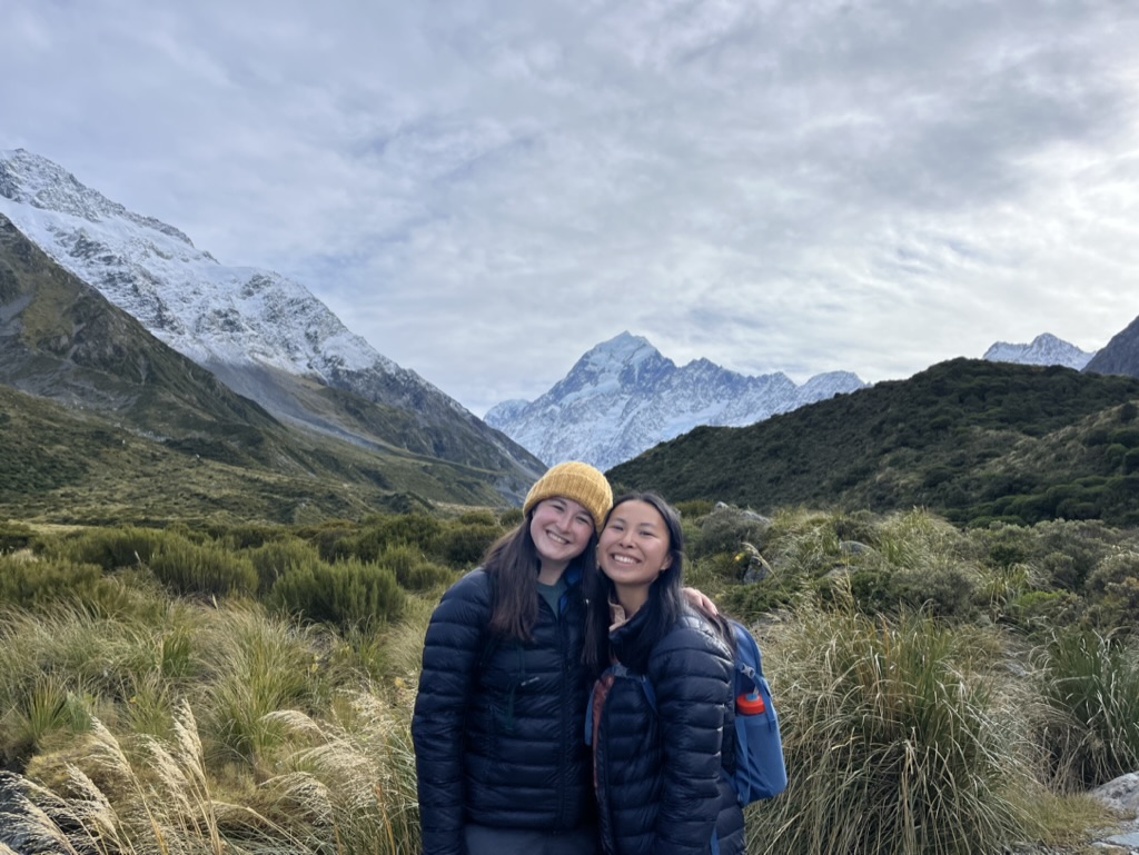 Hannah Lewis and a friend smile for a photo in front of a New Zealand mountainscape.