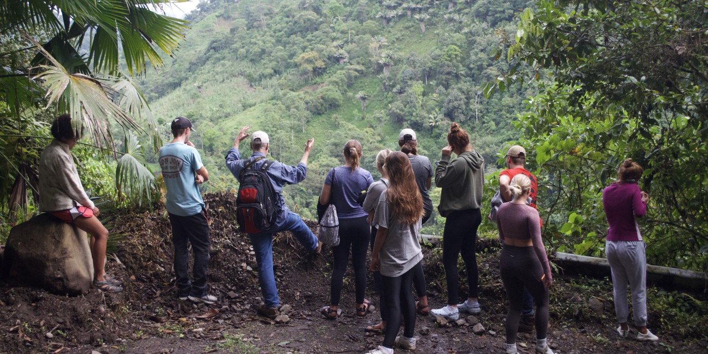 Students in Ecuador look over a stone fence out at a lush mountainscape.