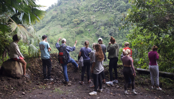 Students in Ecuador look over a stone fence out at a lush mountainscape.