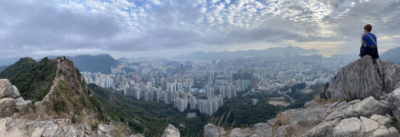 A student sits on a rock looking out at the Hong Kong skyline.