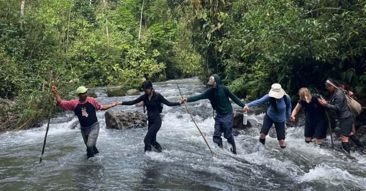 Students led by a guide cross a river with linked arms