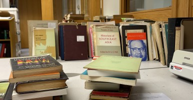 Stacks of books sit on a table in a library.